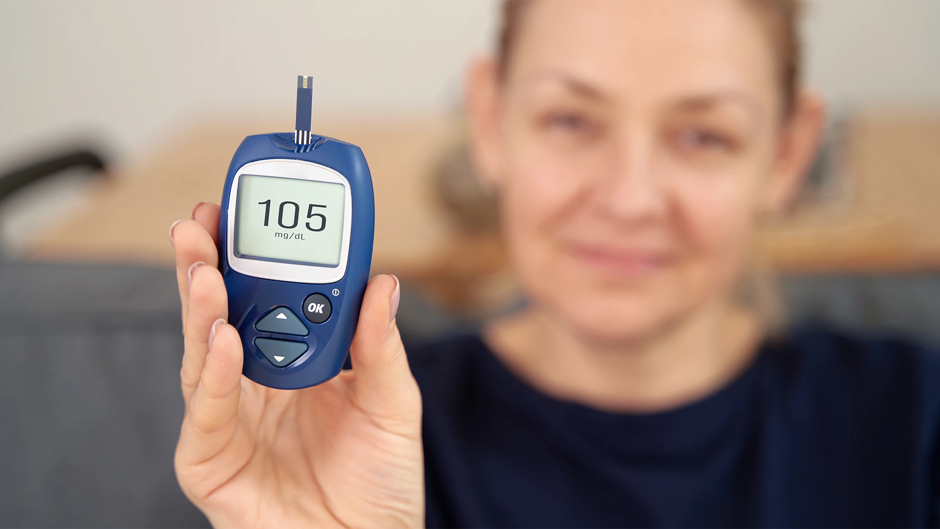 Kobieta trzymająca glukometr pokazujący wynik 105 mg/dl – samokontrola poziomu glukozy we krwi przy hipoglikemii reaktywnej